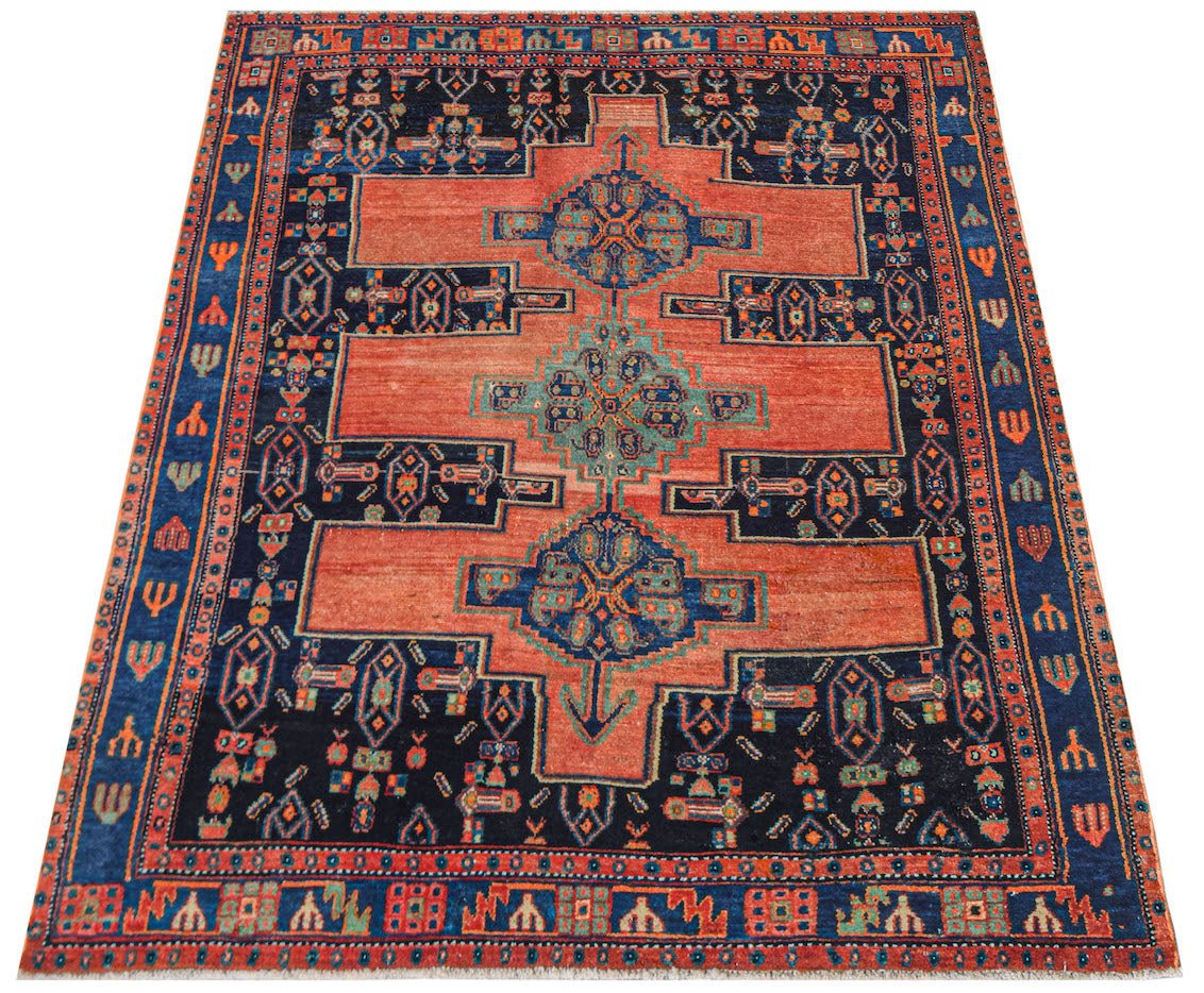A vintage handwoven Persian rug featuring a geometric pattern in shades of orange and navy blue.
