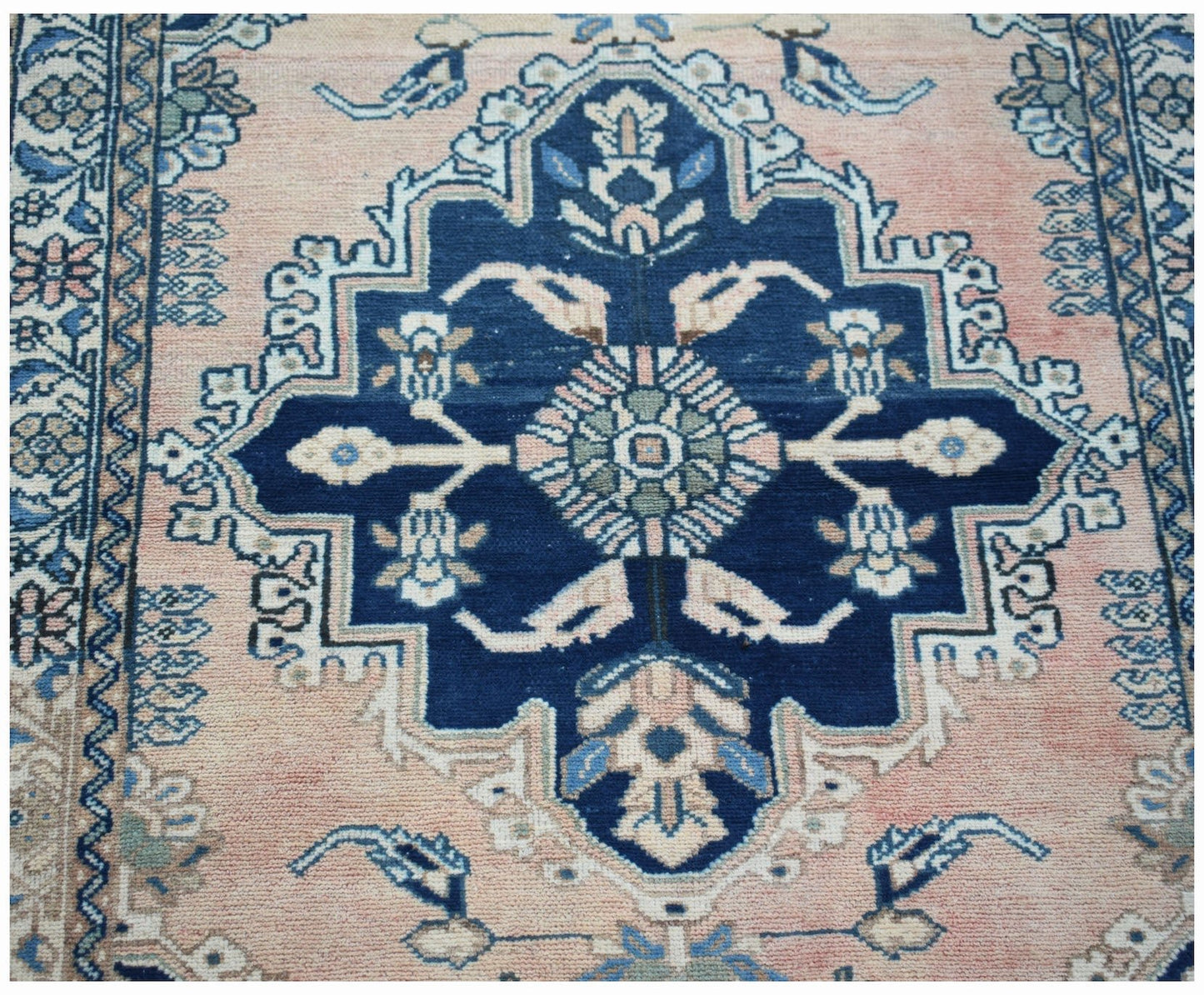 A vintage Persian Sarouk rug featuring a central blue medallion on a soft pink field.