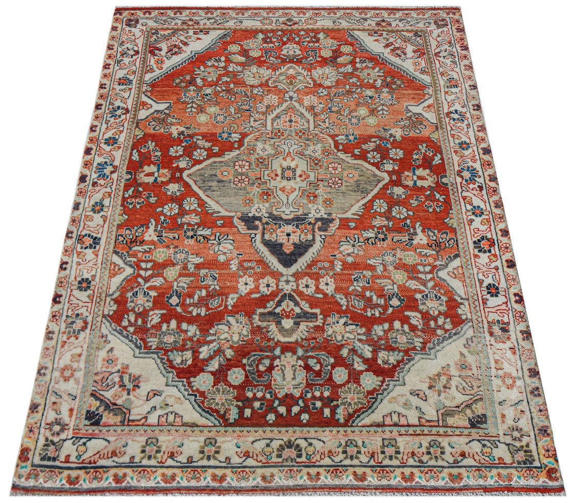 A handwoven vintage Persian rug featuring a central medallion on a red field with floral patterns.