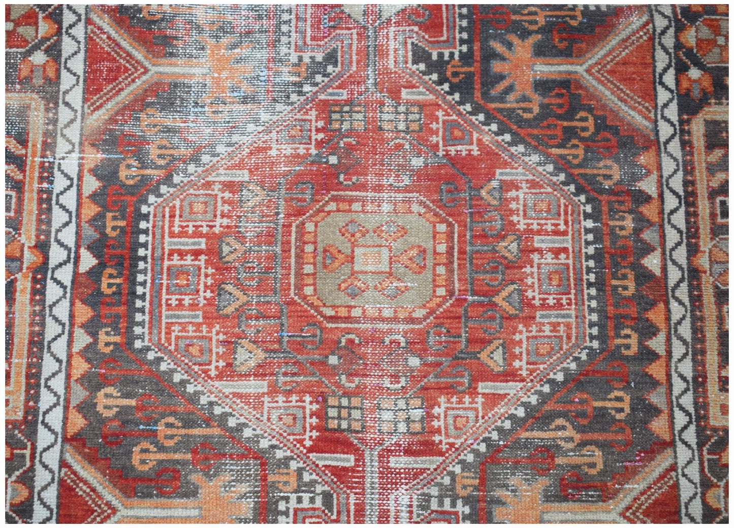 A vintage handwoven Persian rug featuring a geometric medallion pattern in red, grey, and orange.