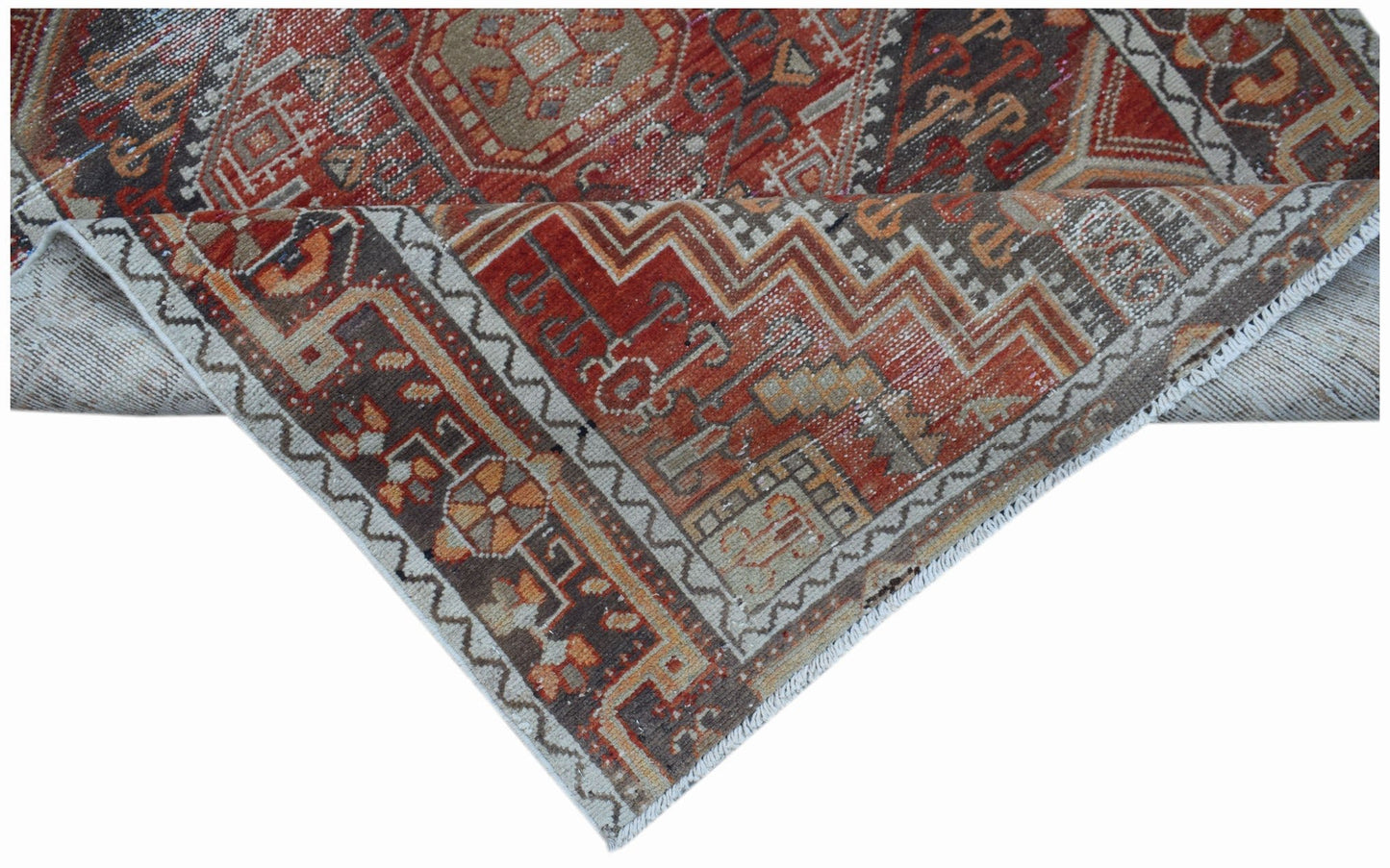 A handwoven vintage Persian rug featuring intricate geometric patterns in red, brown, and beige.