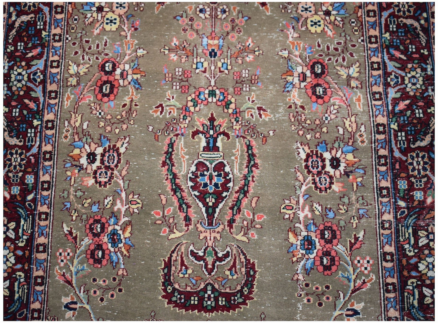 A vintage handwoven Persian rug featuring a central floral vase motif on a muted olive background.