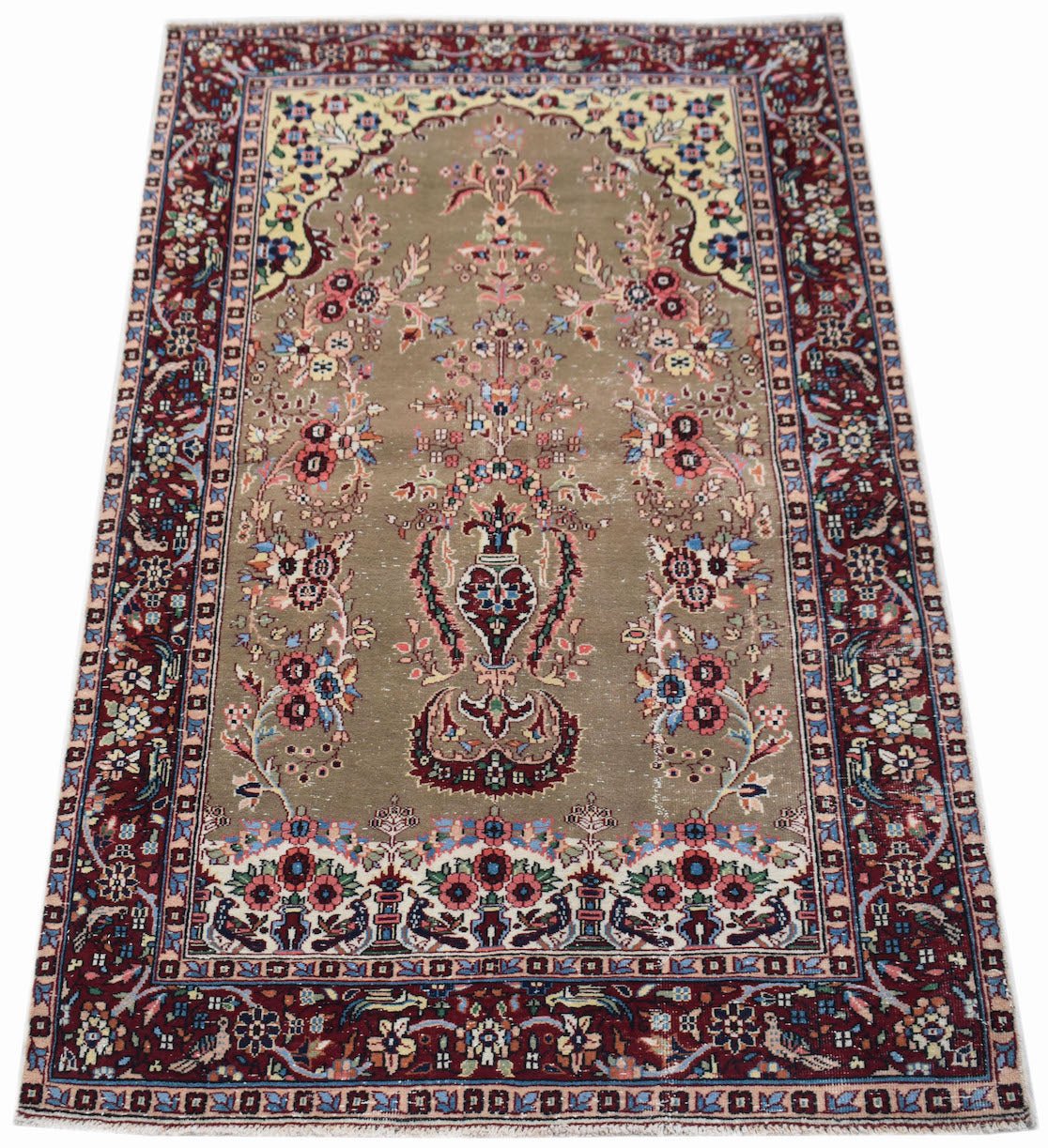 A vintage handwoven Persian rug featuring a central floral vase motif on a taupe field.