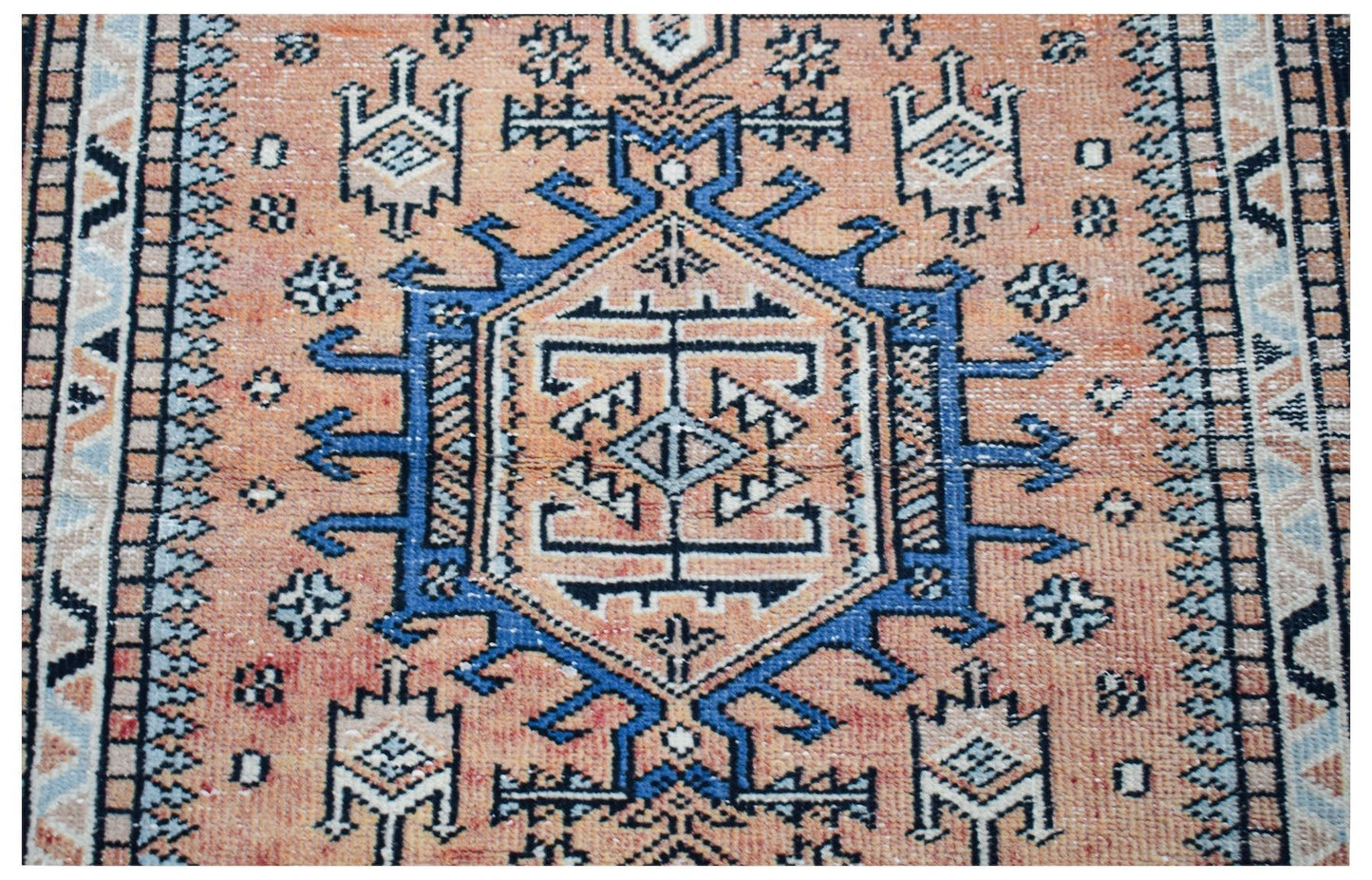 A handwoven vintage Persian rug featuring a geometric blue medallion on a peach background.