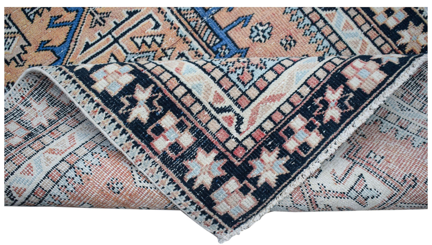 A vintage handwoven Persian rug featuring geometric patterns in shades of peach, blue, and black.