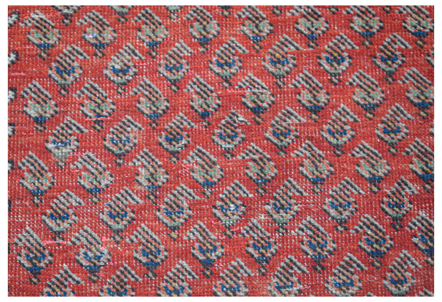 A vintage handwoven Persian rug featuring a repeating paisley pattern on a vibrant red background.