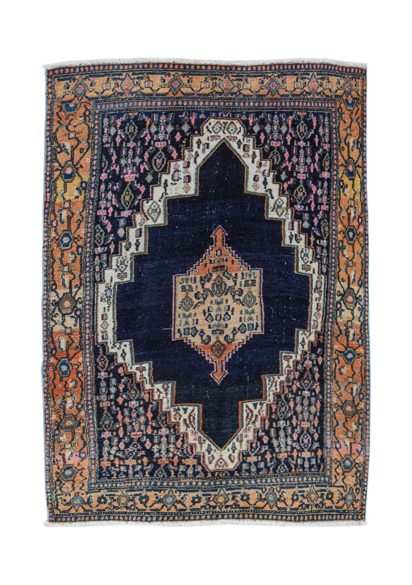 A vintage handwoven Persian rug featuring a dark blue central medallion on an orange patterned field.