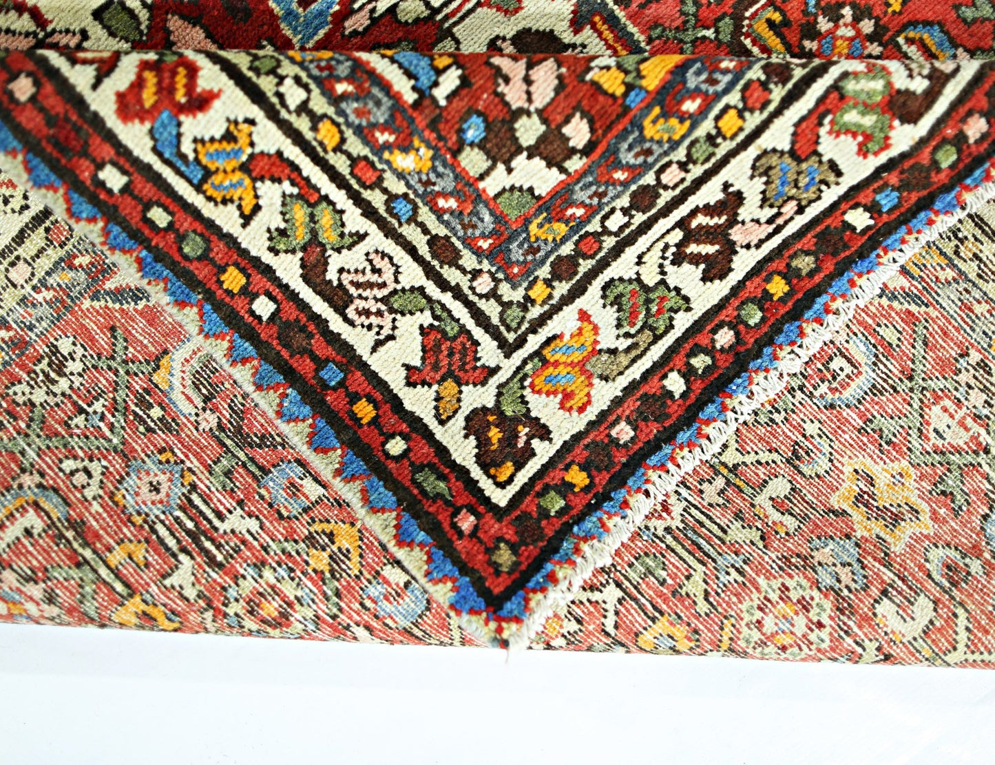 A folded vintage Persian Sarouk rug featuring intricate floral patterns in red, blue, and cream.