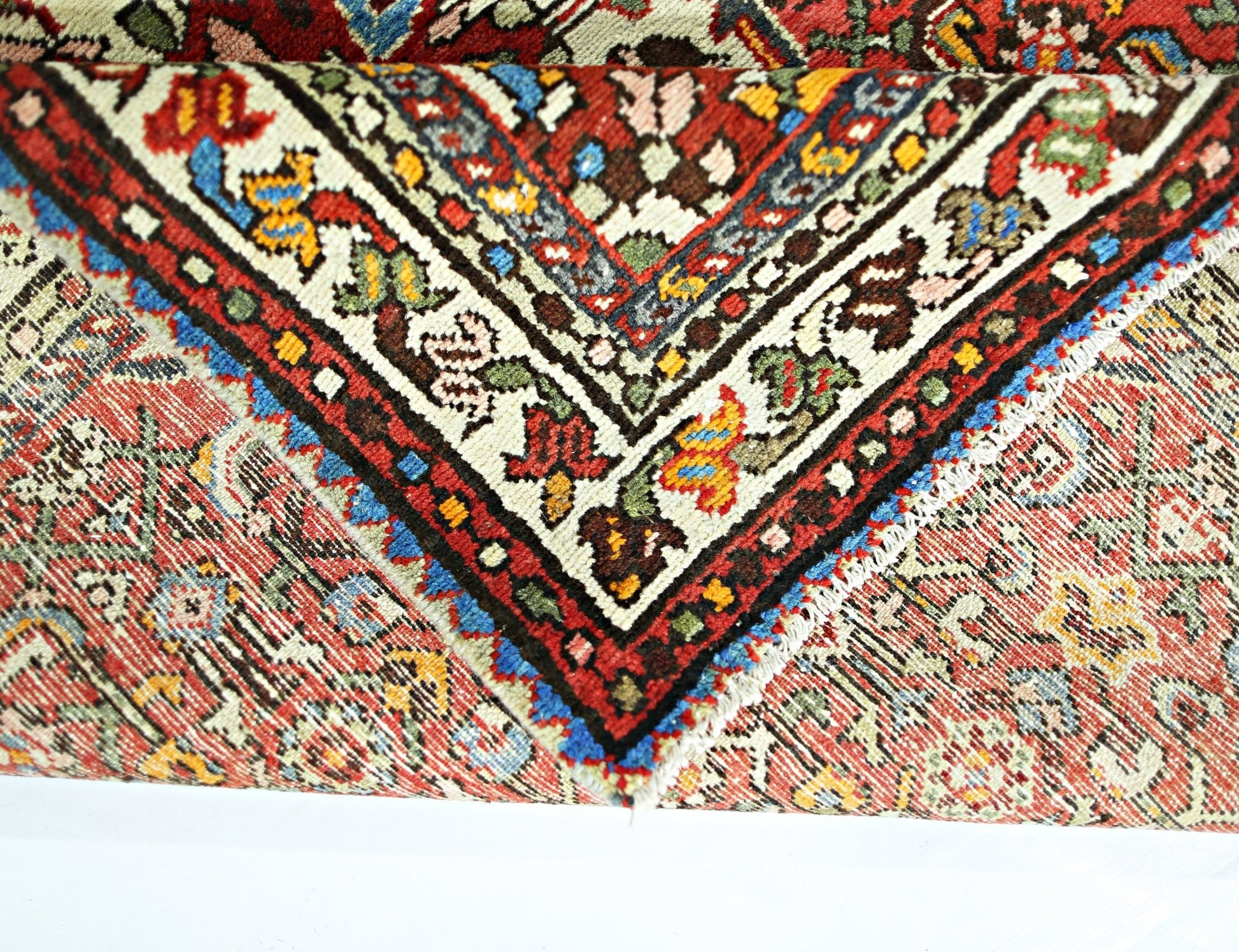 A folded vintage Persian Sarouk rug featuring intricate floral patterns in red, blue, and cream.