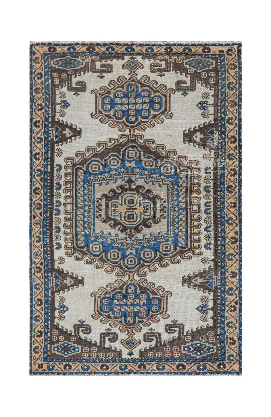 A handwoven vintage Persian rug featuring a central blue medallion on a cream field.