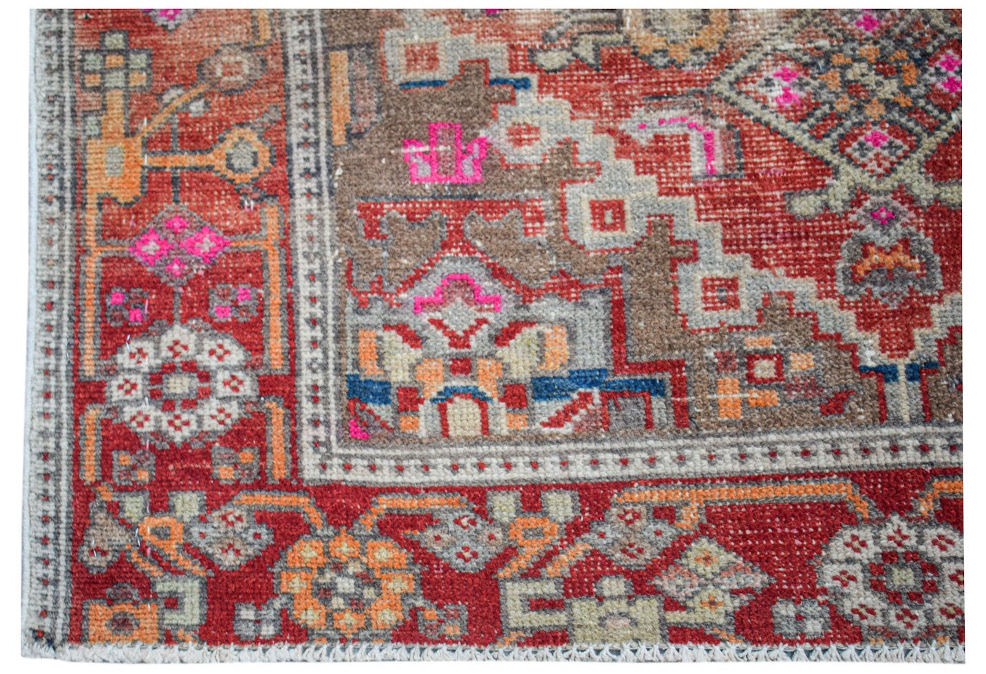 A handwoven vintage Persian rug featuring a geometric pattern in red, brown, and bright pink.