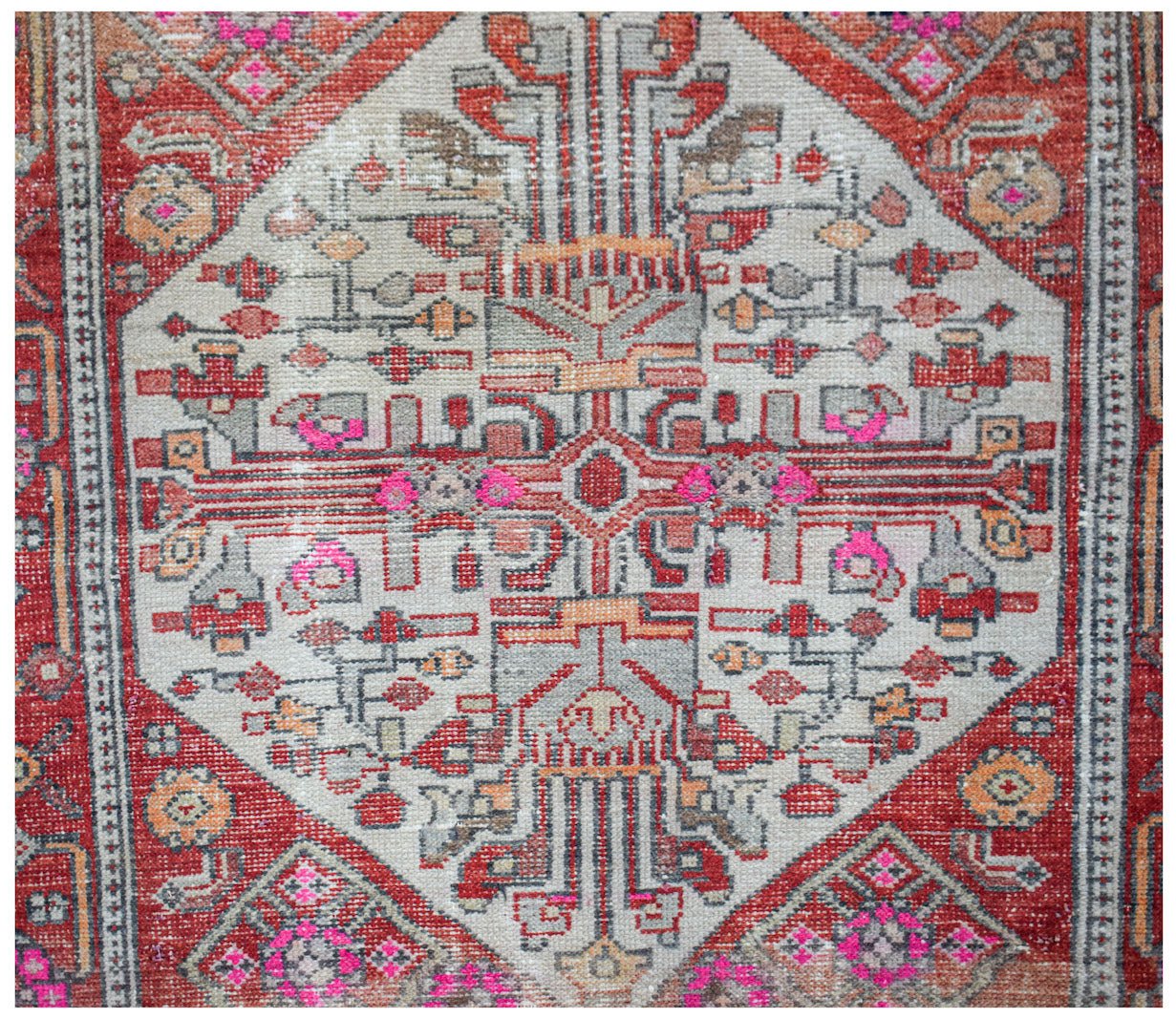 A handwoven vintage Persian rug featuring a geometric diamond medallion in red, grey, and pink.
