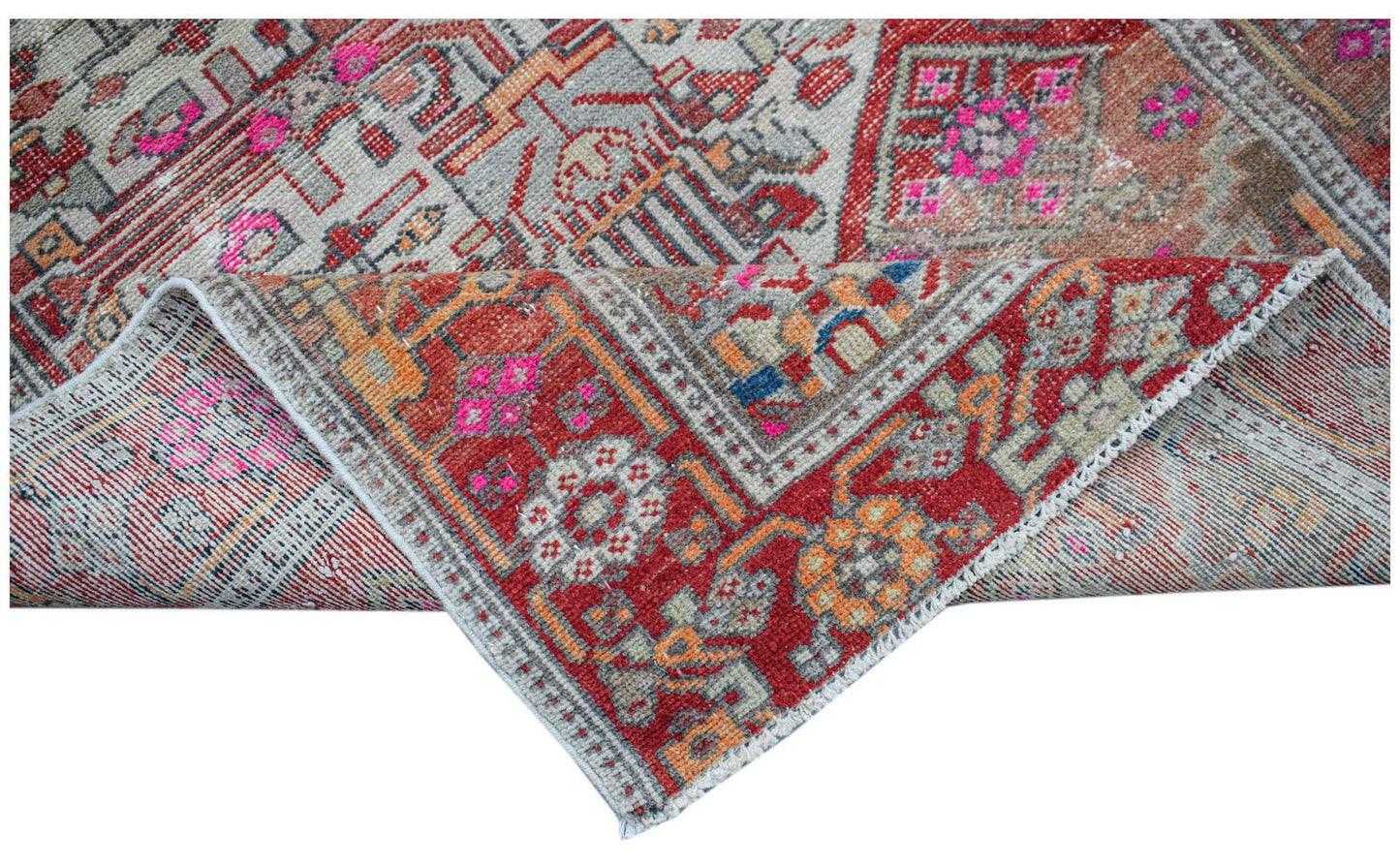 A vintage handwoven Persian rug featuring a geometric pattern in red, grey, and bright pink.