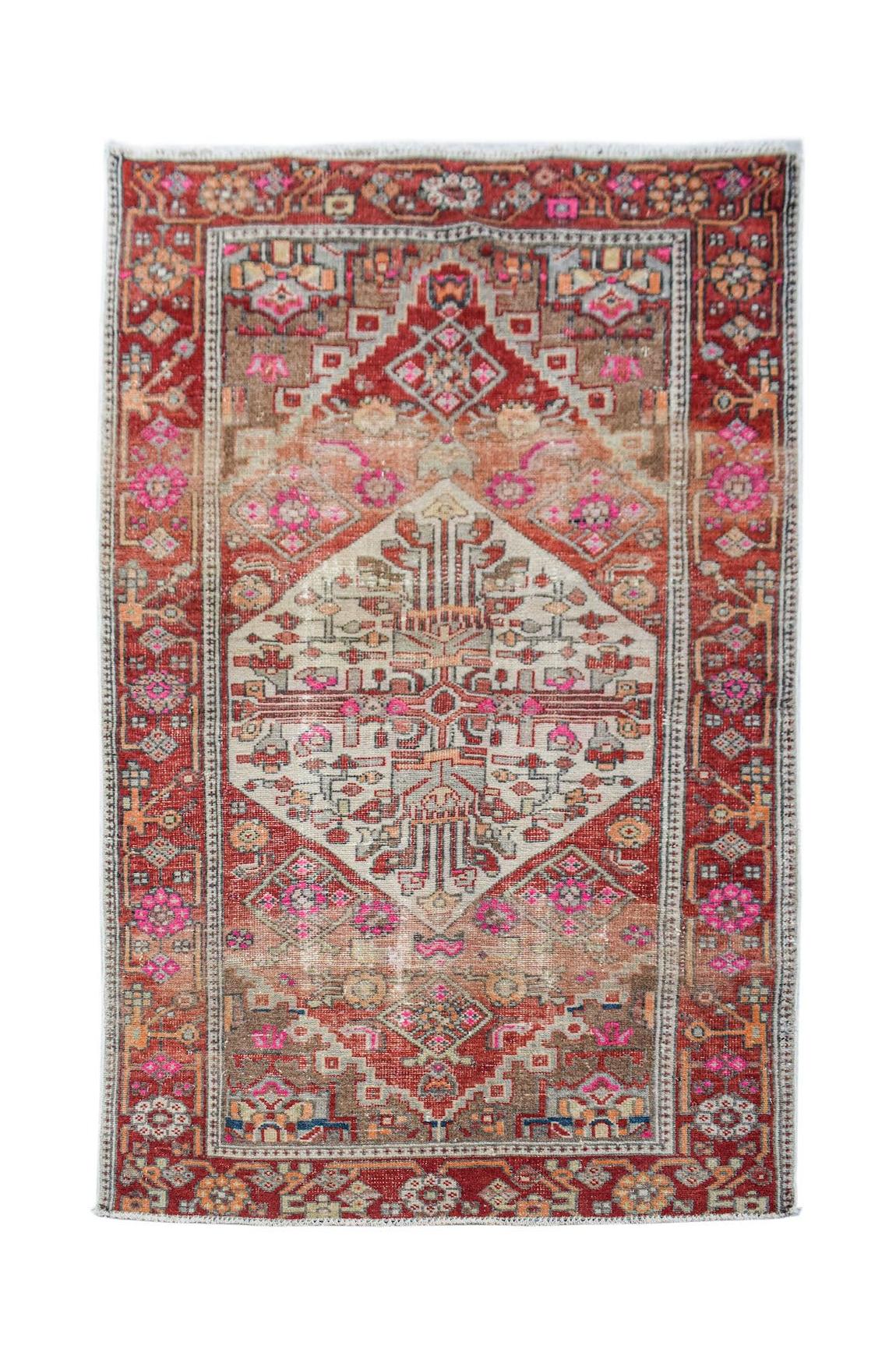A vintage handwoven Persian rug featuring a central geometric medallion in red, pink, and beige.