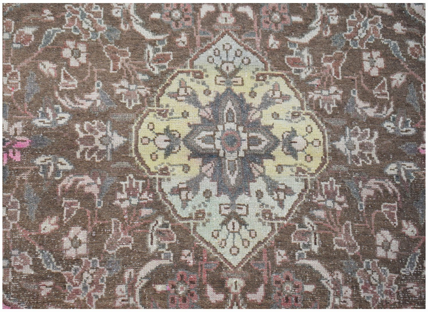 A vintage handwoven Persian rug featuring a central yellow medallion on a brown floral field.