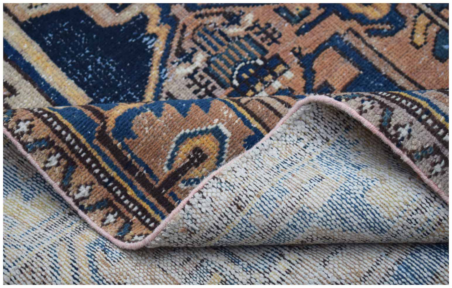 A folded vintage Persian rug featuring a traditional geometric pattern in blue and tan tones.