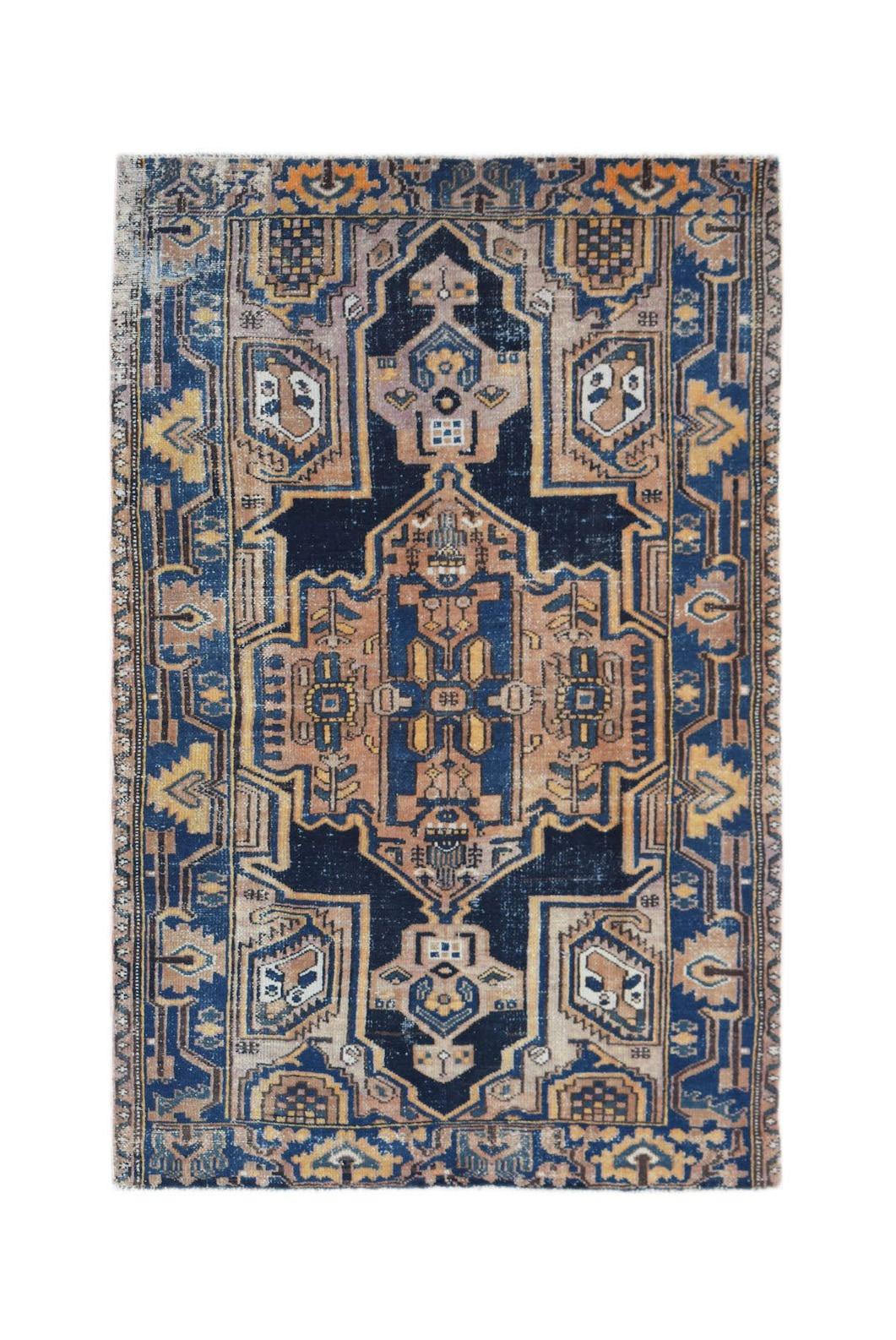 A handwoven vintage Persian rug featuring a geometric medallion pattern in blue, tan, and gold.