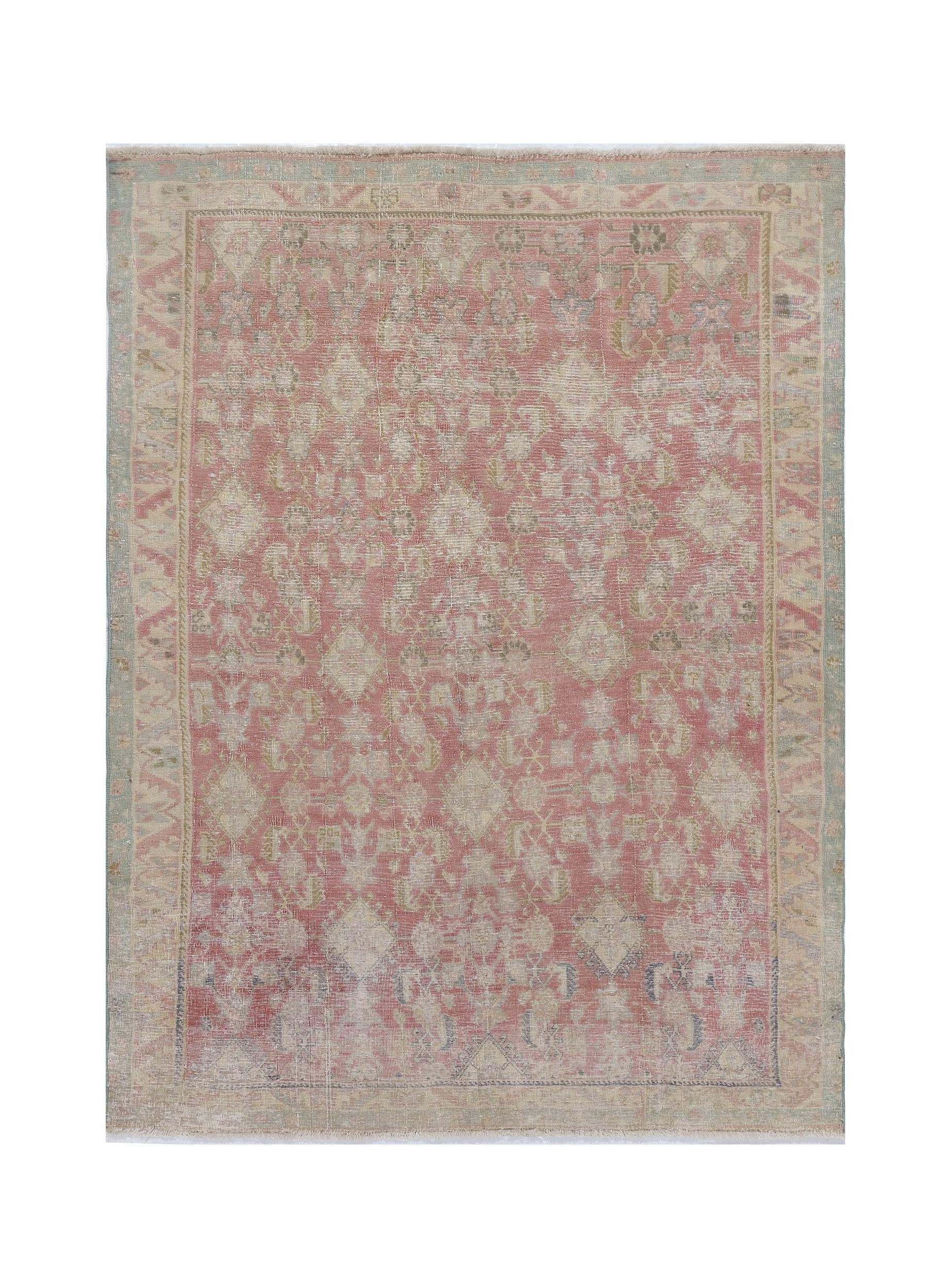 A vintage handmade Persian rug featuring a faded pink and cream geometric floral pattern.