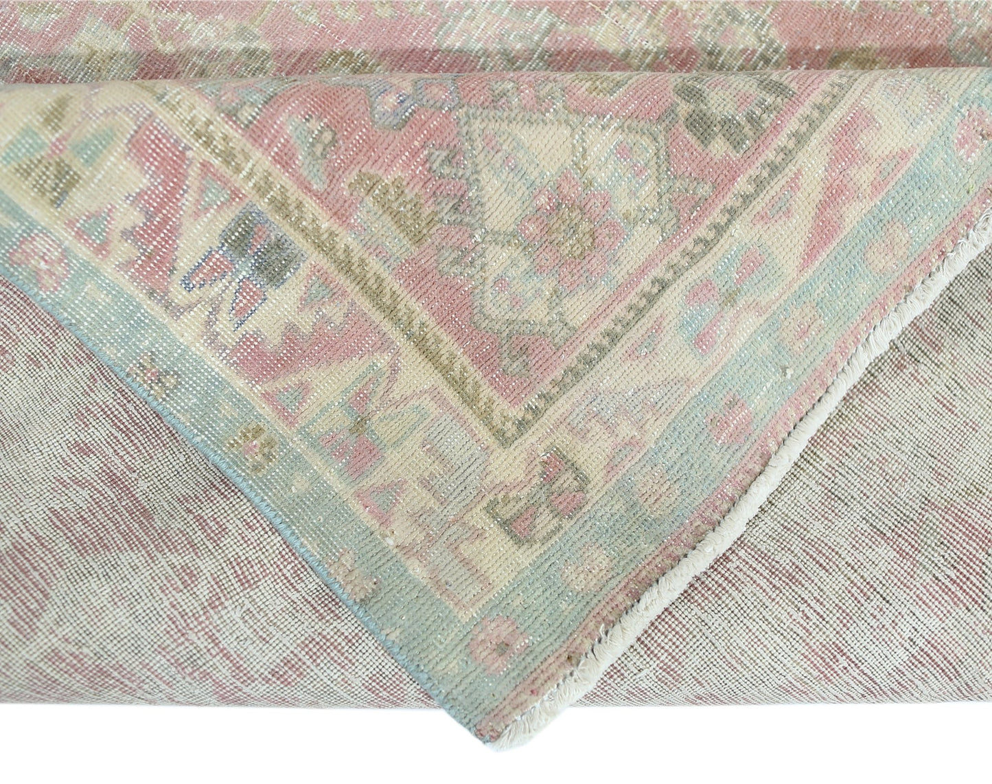 A folded vintage Persian rug featuring a pink and blue floral pattern on a wool and cotton base.
