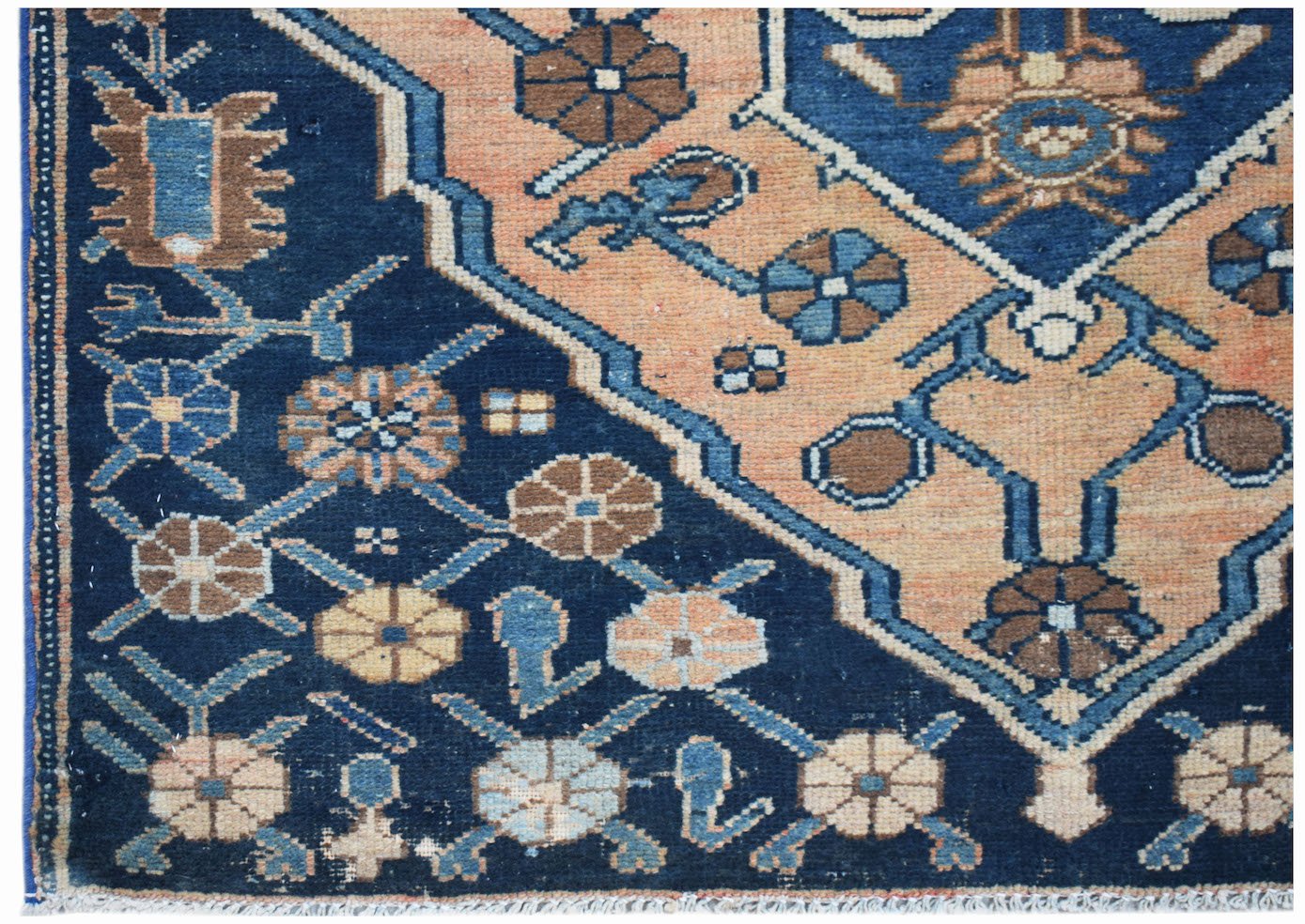 A vintage handwoven Persian rug featuring a geometric floral pattern in blue and peach tones.