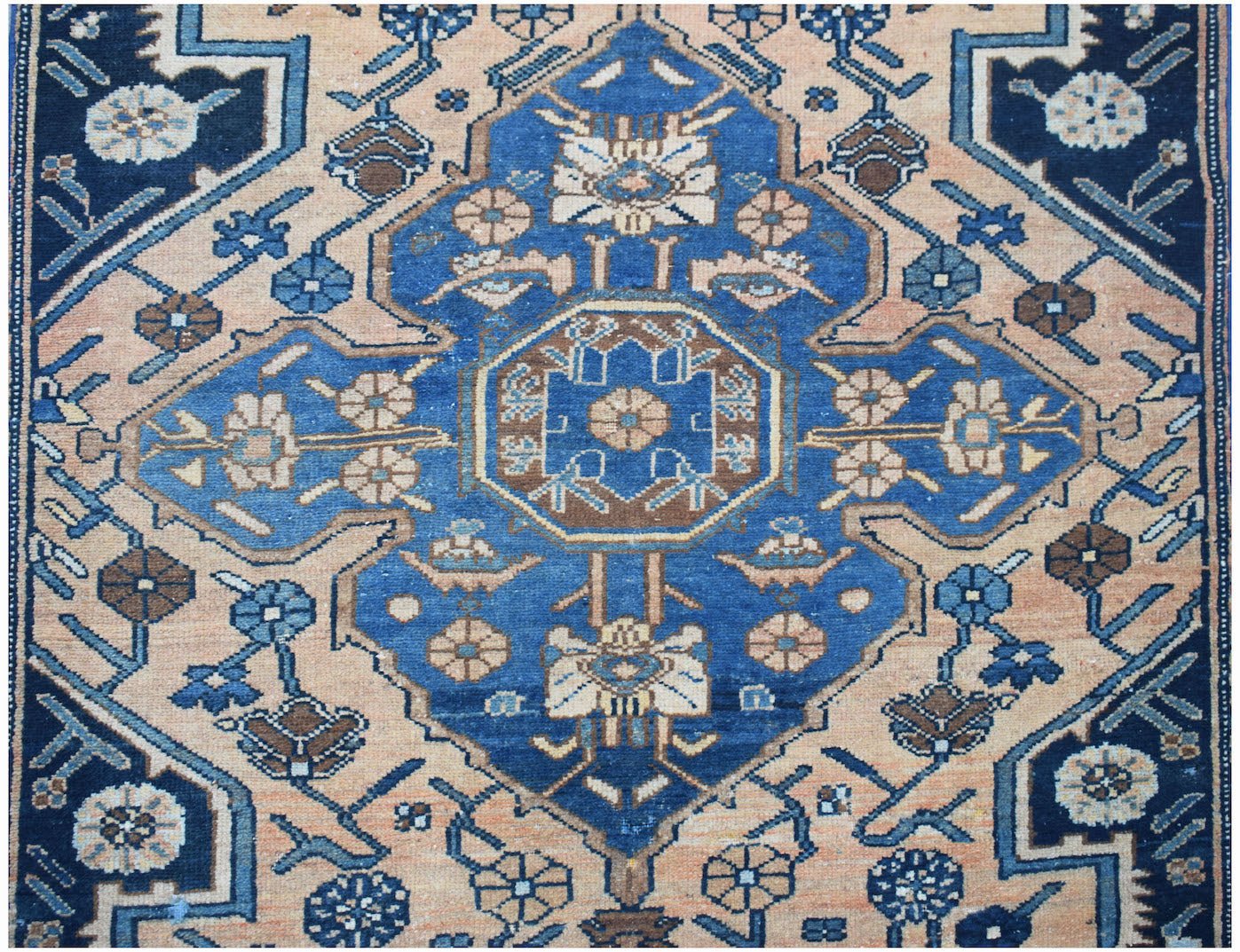 A vintage handwoven Persian rug featuring a blue central medallion on a peach field with floral motifs.