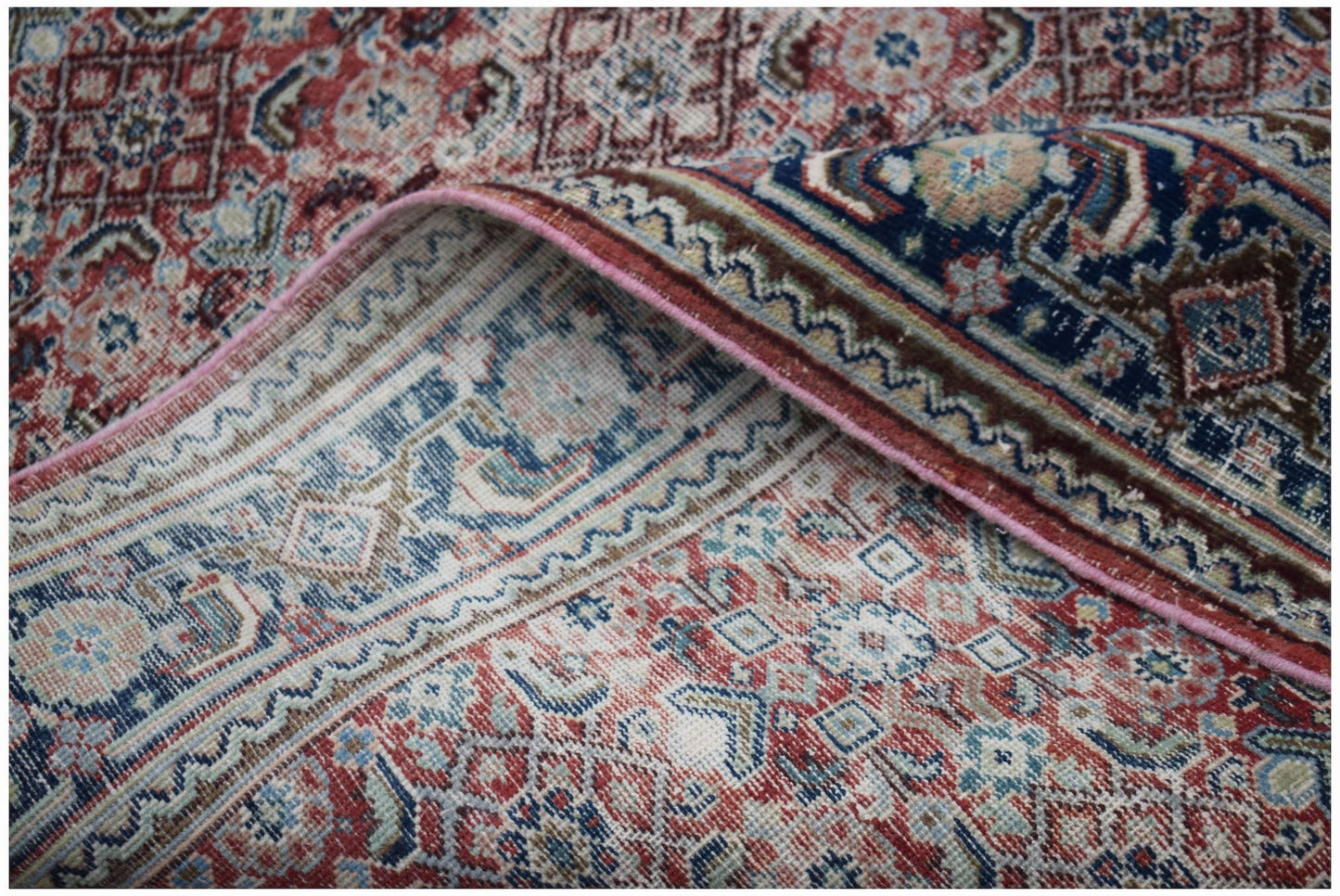 A vintage handwoven Persian wool rug featuring intricate geometric patterns in red and blue.