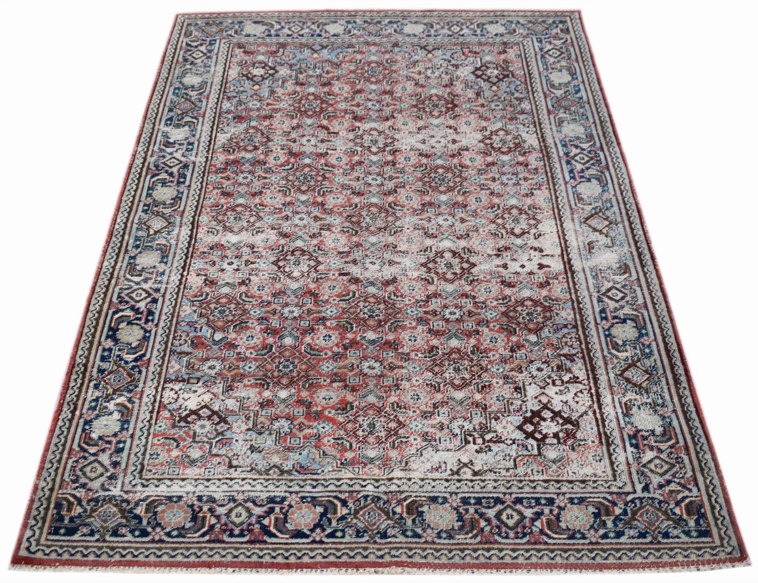 A vintage handwoven Persian rug featuring a faded red and blue geometric pattern.