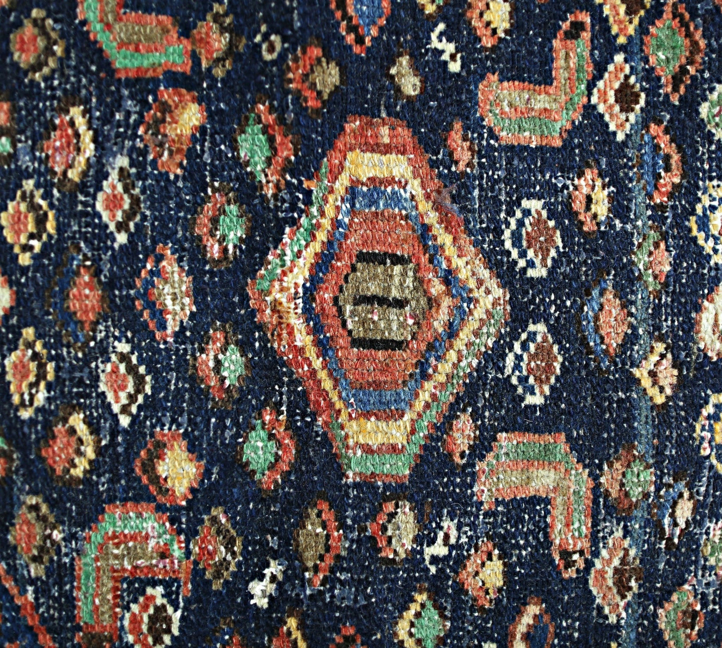 A close-up of a vintage Persian Hamadan rug featuring a geometric medallion on a dark blue field.