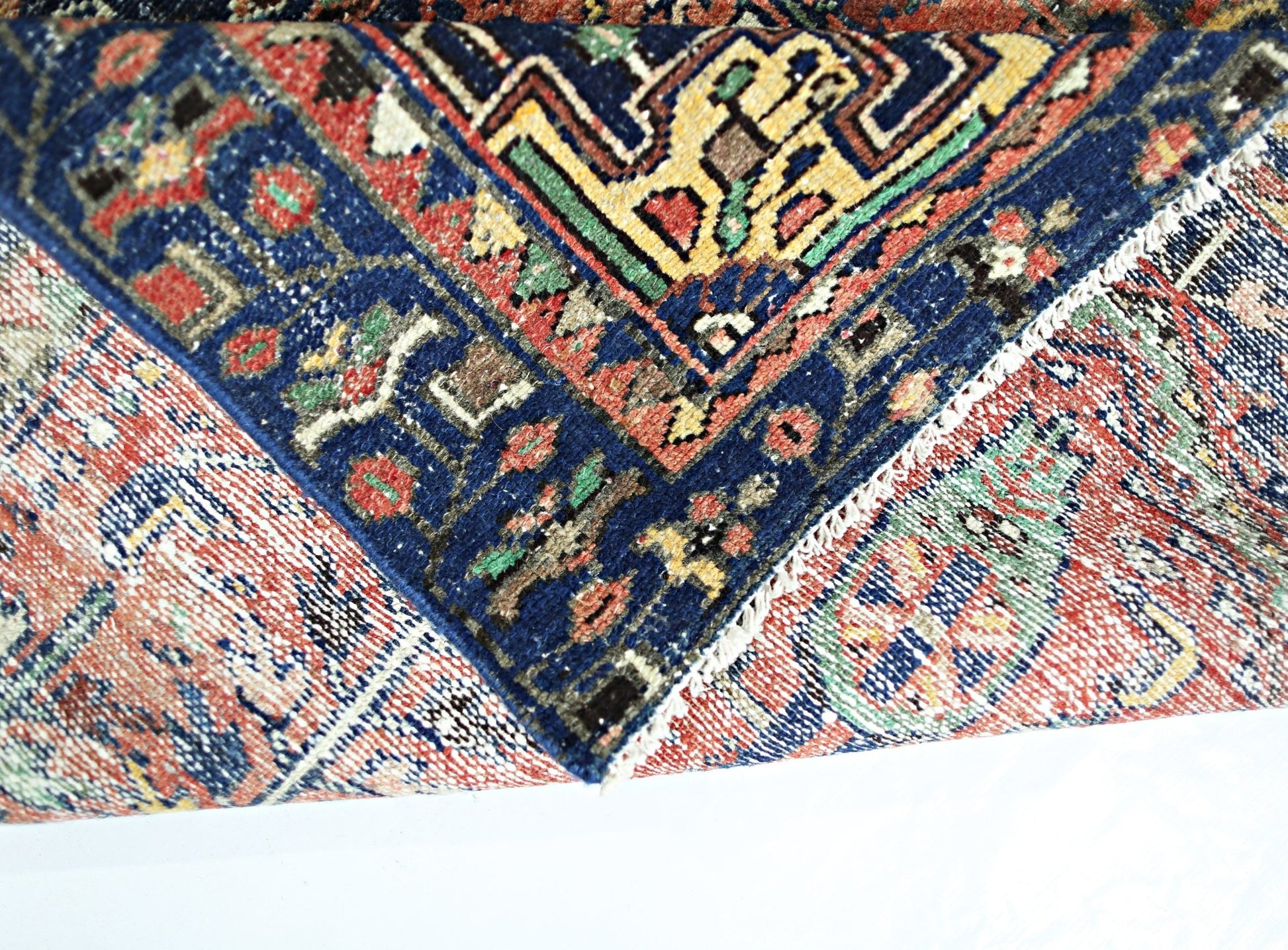 A folded vintage Persian Hamadan rug featuring intricate geometric patterns in red, blue, and gold.