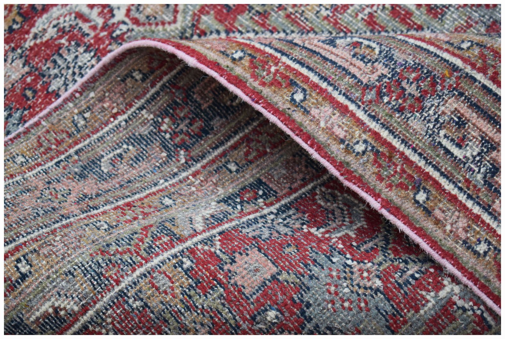 A vintage Persian rug with a distressed red and blue floral pattern and a pink bound edge.