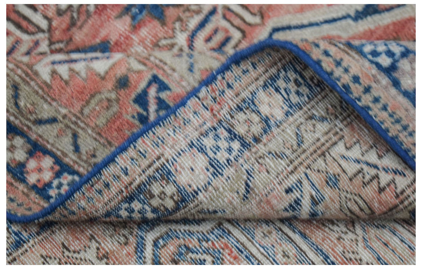 A vintage handwoven Persian rug featuring a faded floral pattern in shades of blue and coral.
