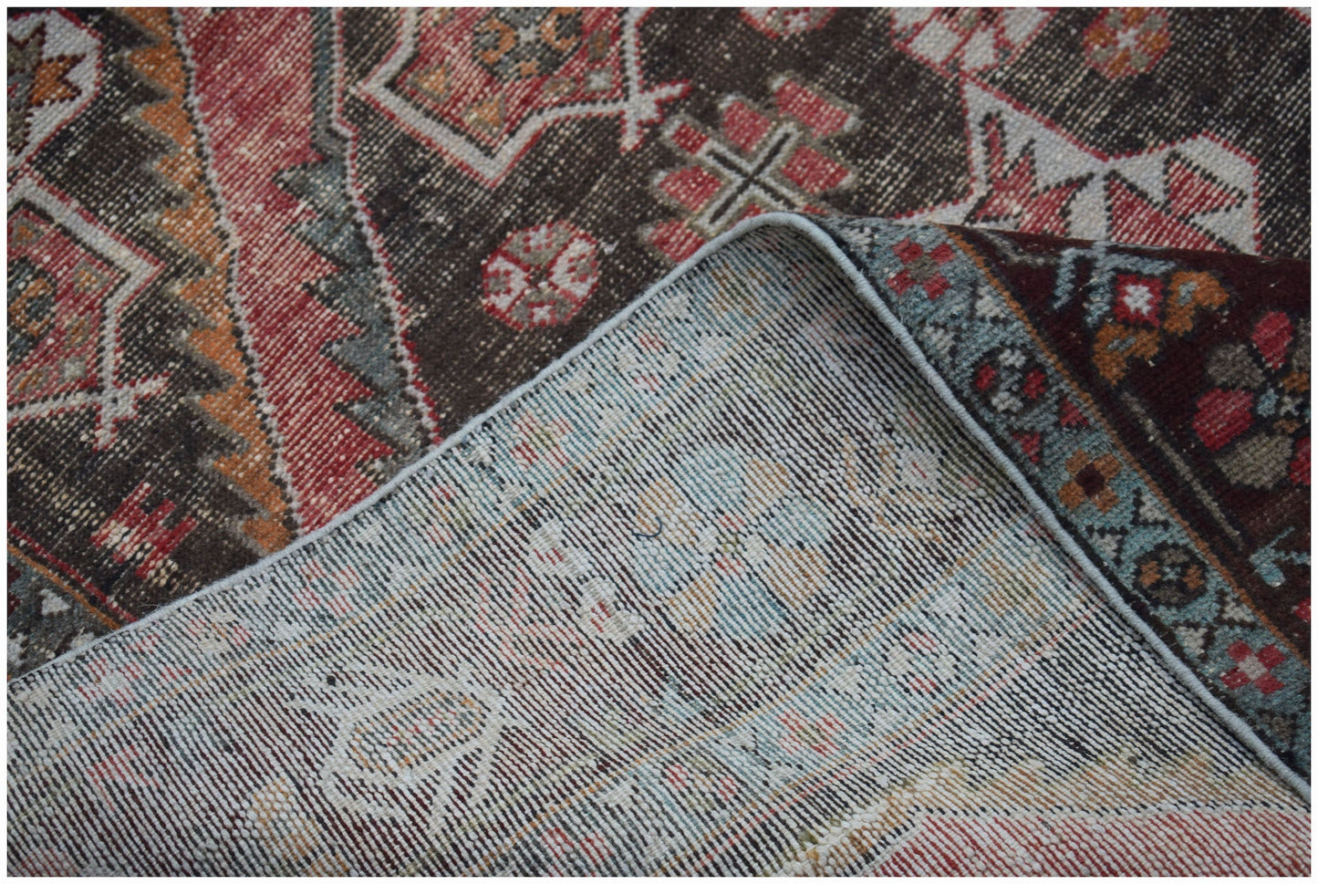 A corner of a vintage Persian Hamadan rug is folded back to show its handwoven wool construction.