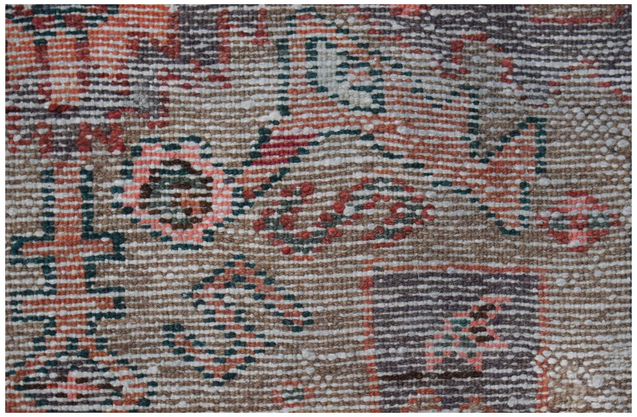 A close-up view of a handwoven vintage Persian rug featuring faded geometric and floral patterns.