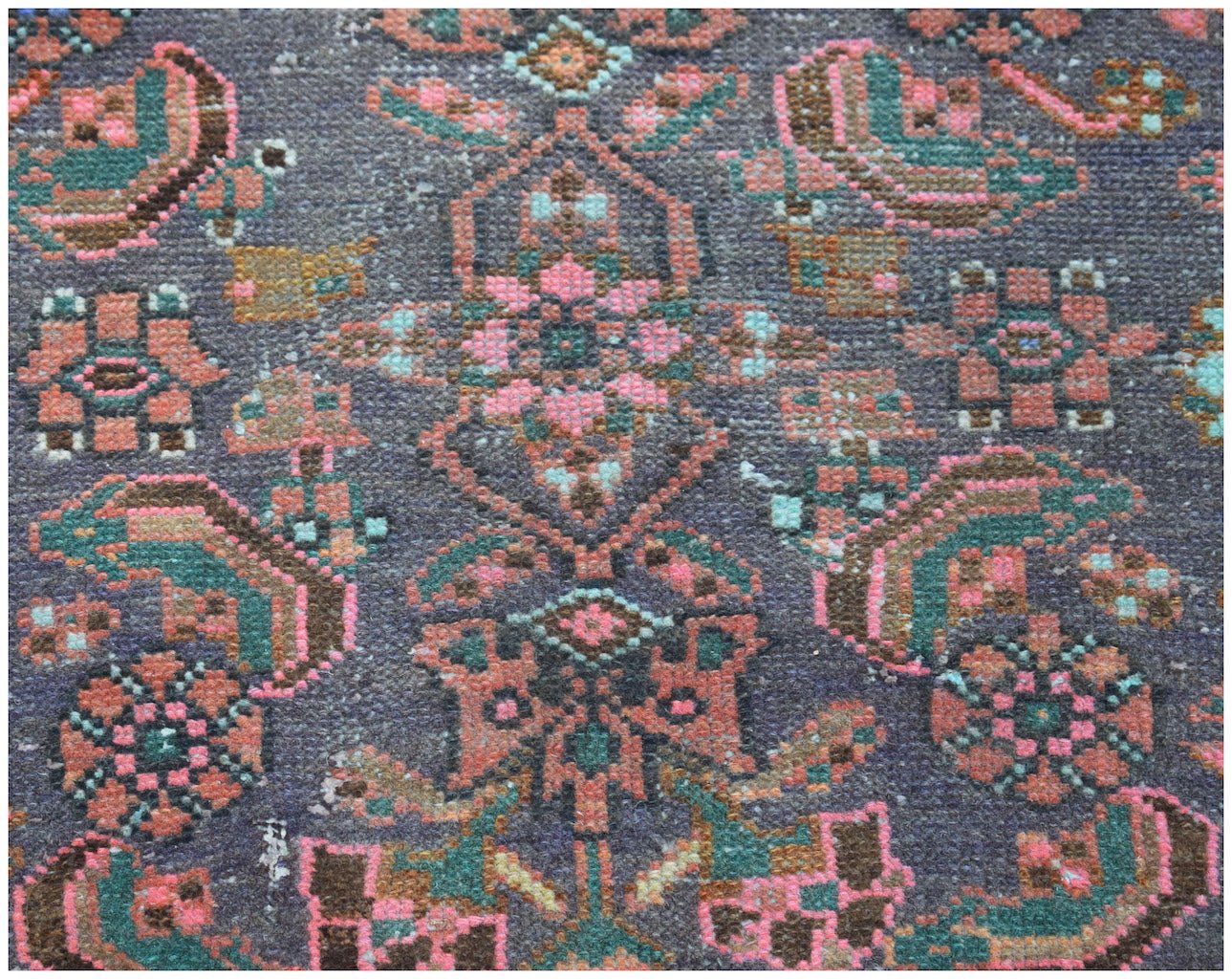 A vintage handwoven Persian rug featuring a detailed floral pattern in pink, green, and brown.