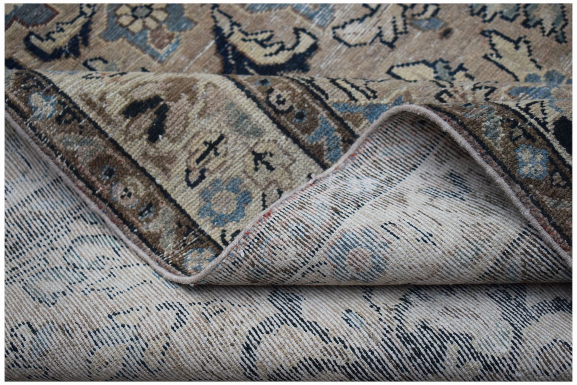 A vintage Persian Sarouk rug with a folded corner showing its handwoven wool construction.
