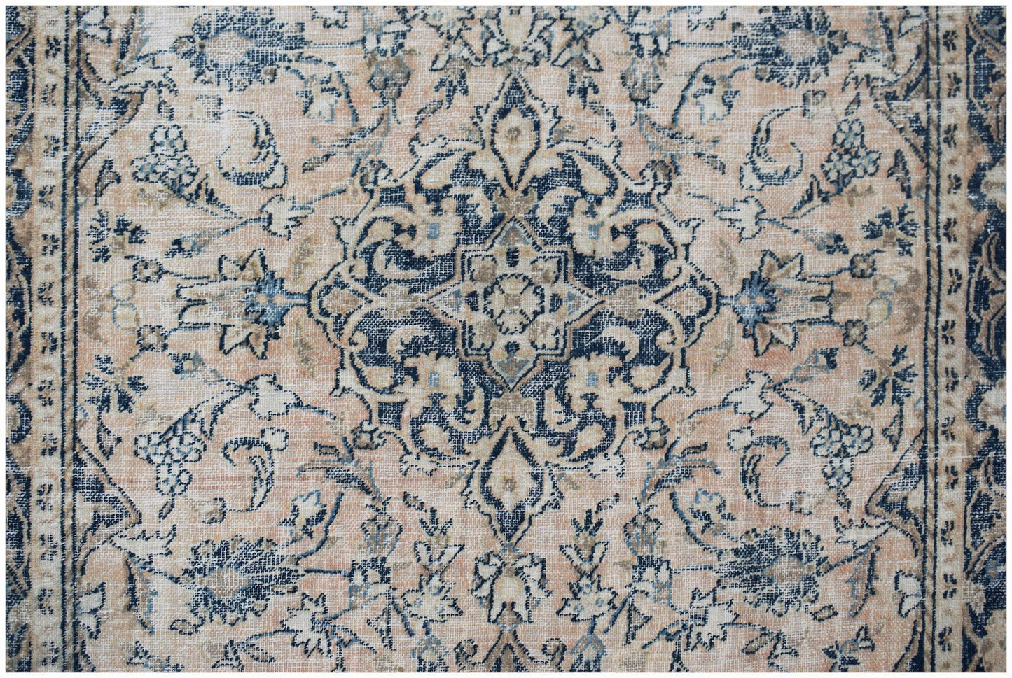 A vintage Persian rug featuring a central floral medallion in navy blue on a faded peach background.