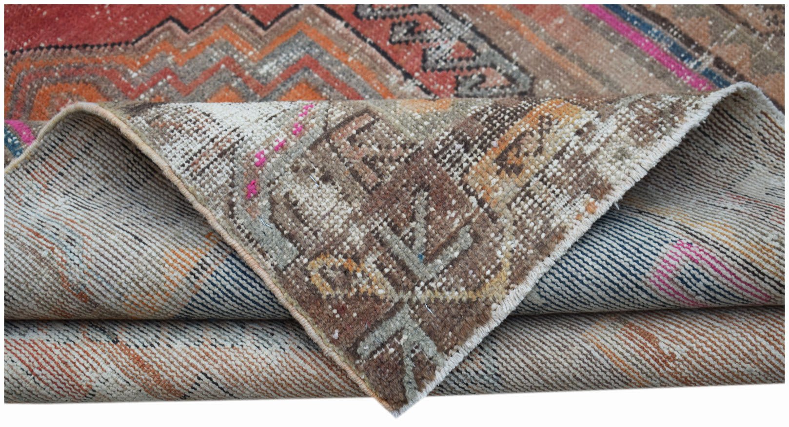 A folded vintage Persian rug featuring geometric patterns in muted orange, brown, and blue tones.