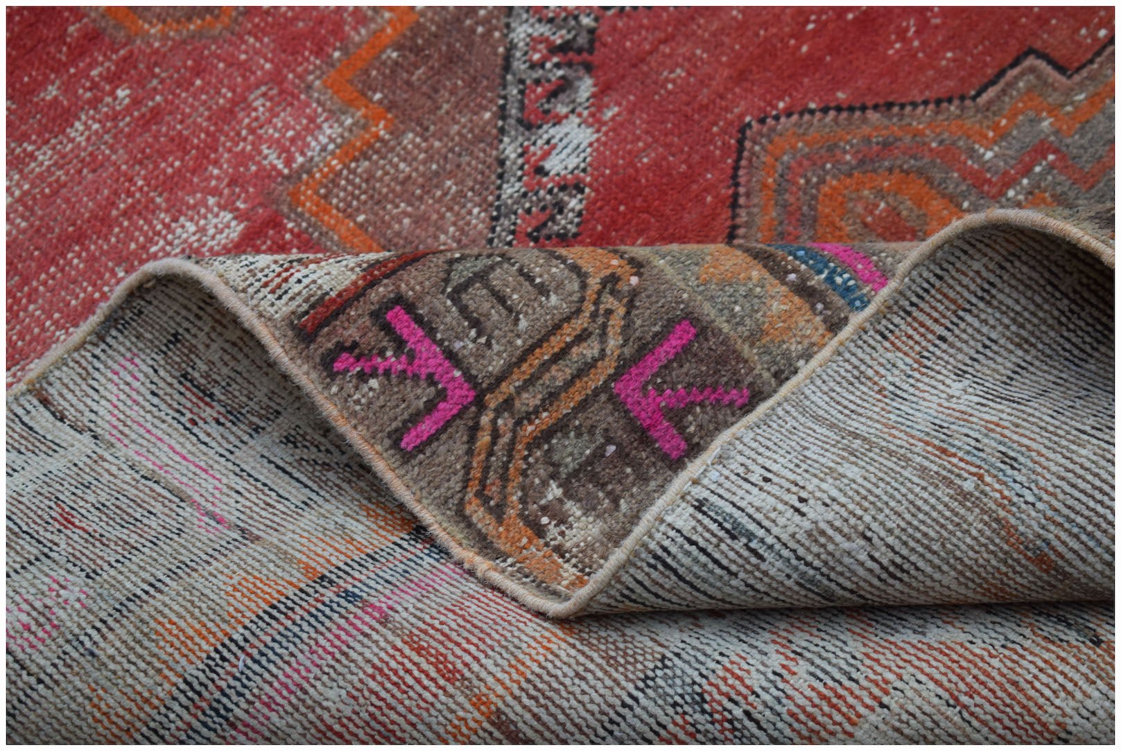 A vintage handwoven Persian rug featuring a distressed red, brown, and orange geometric pattern.