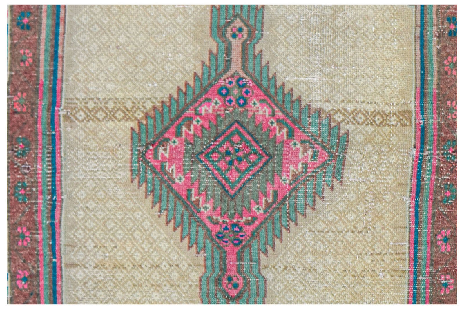Vintage Persian rug with diamond and geometric patterns in pink, teal, and beige.