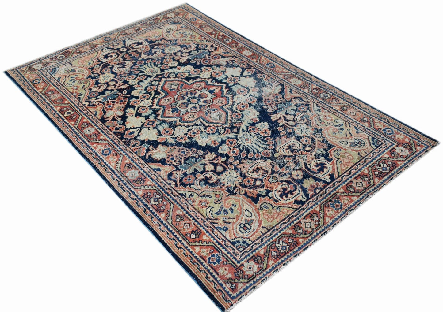 A vintage handwoven Persian rug featuring a central floral medallion on a dark blue background.