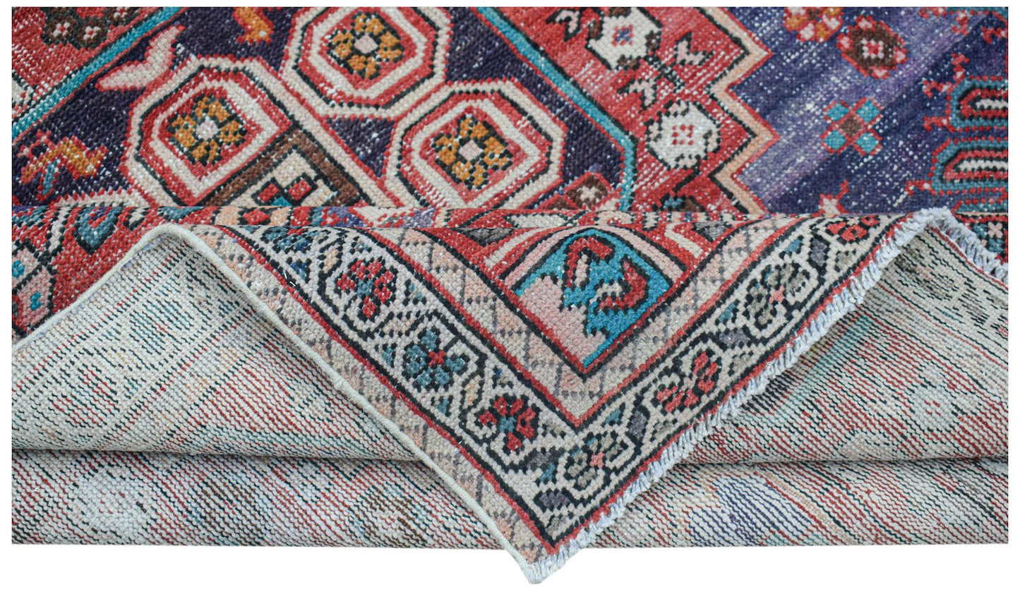 A handwoven vintage Persian rug featuring geometric patterns in red, blue, and cream tones.
