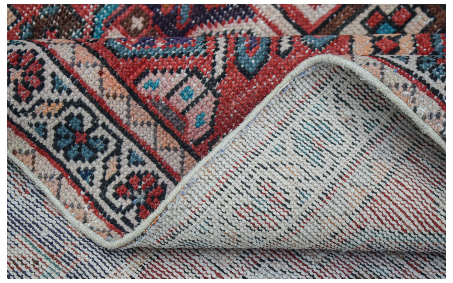 A handwoven vintage Persian rug with a colorful geometric pattern and a visible cotton base.