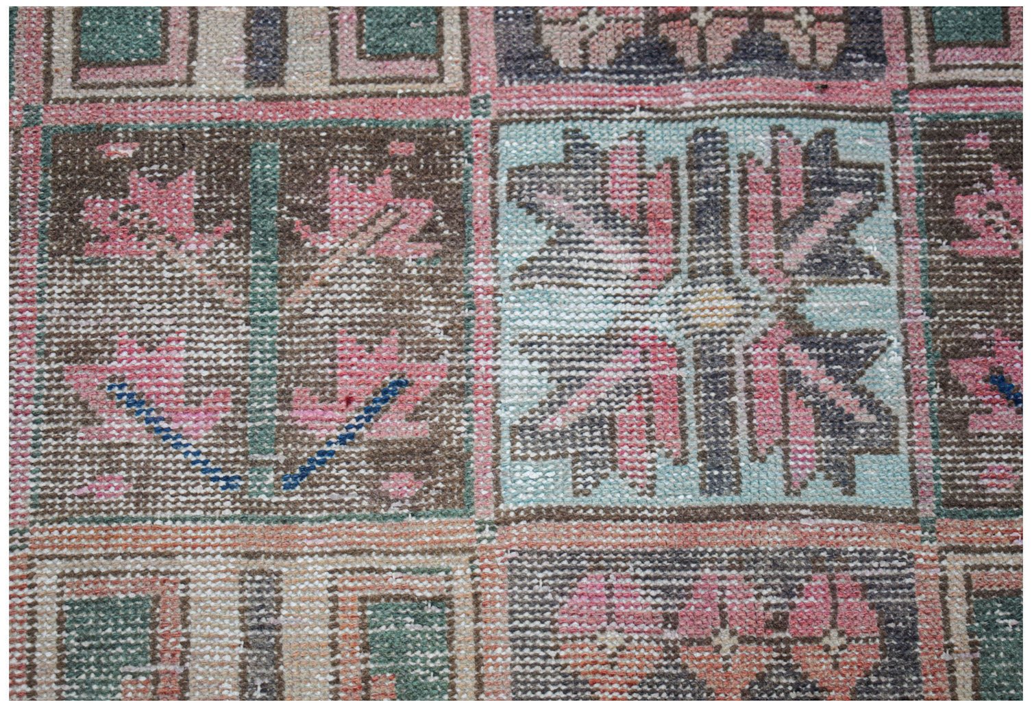 A vintage handwoven Persian rug featuring a geometric grid pattern in muted pink, blue, and brown.