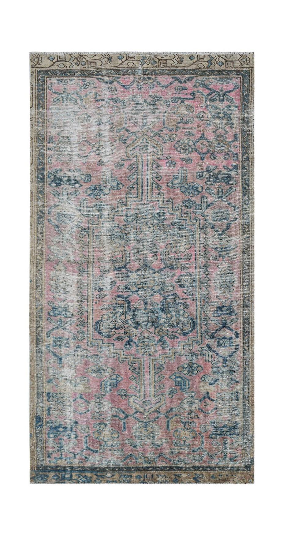 A vintage handwoven Persian rug featuring a faded pink and blue floral medallion pattern.