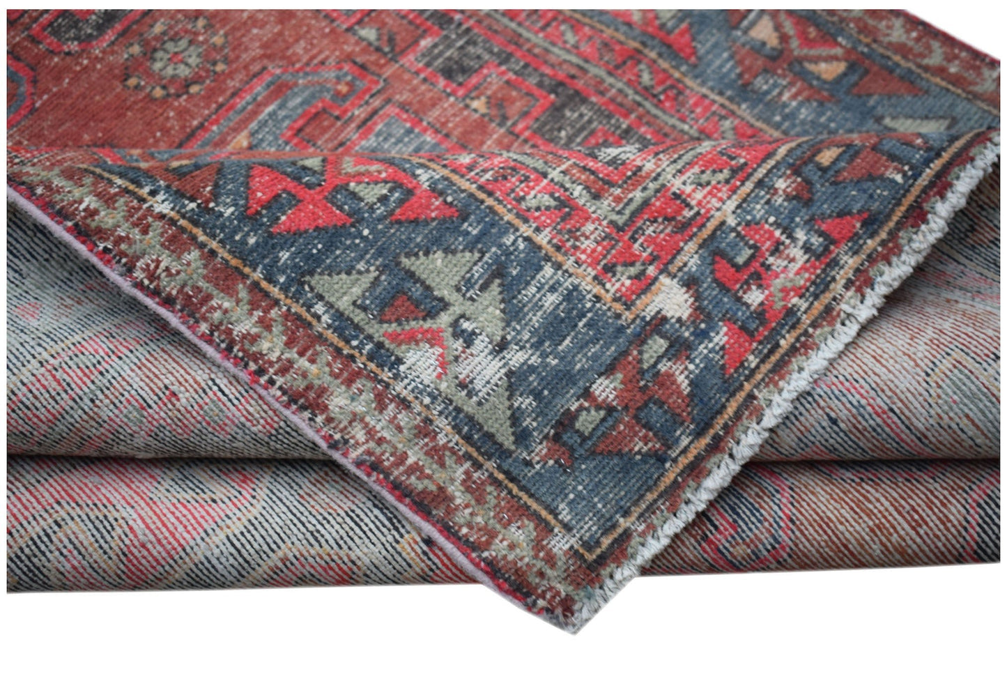 A vintage handwoven Persian rug featuring a distressed red and blue geometric pattern.