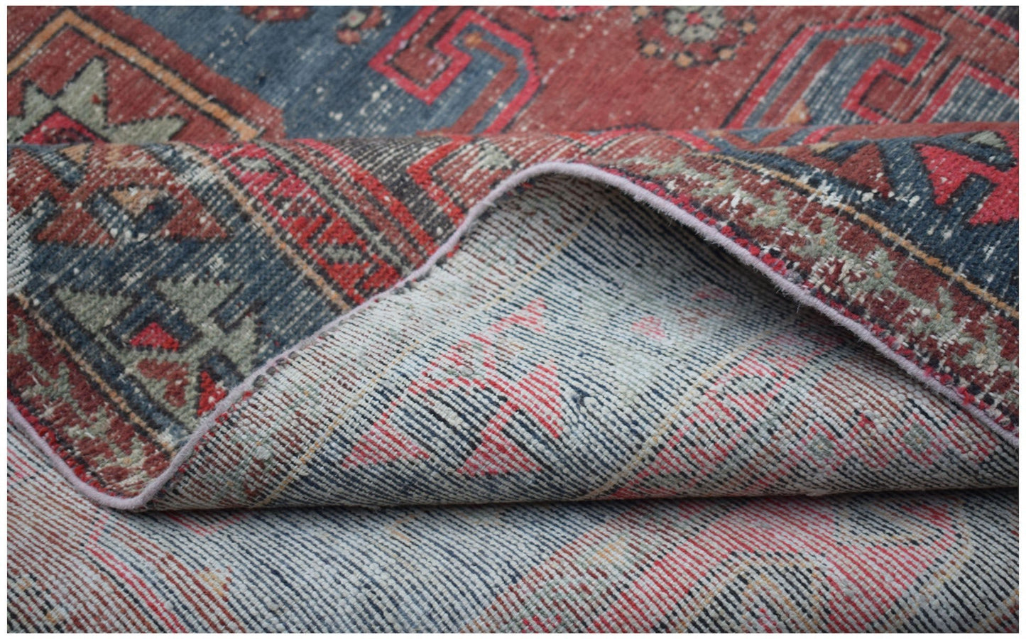 A handwoven vintage Persian rug featuring a distressed red and blue geometric pattern.