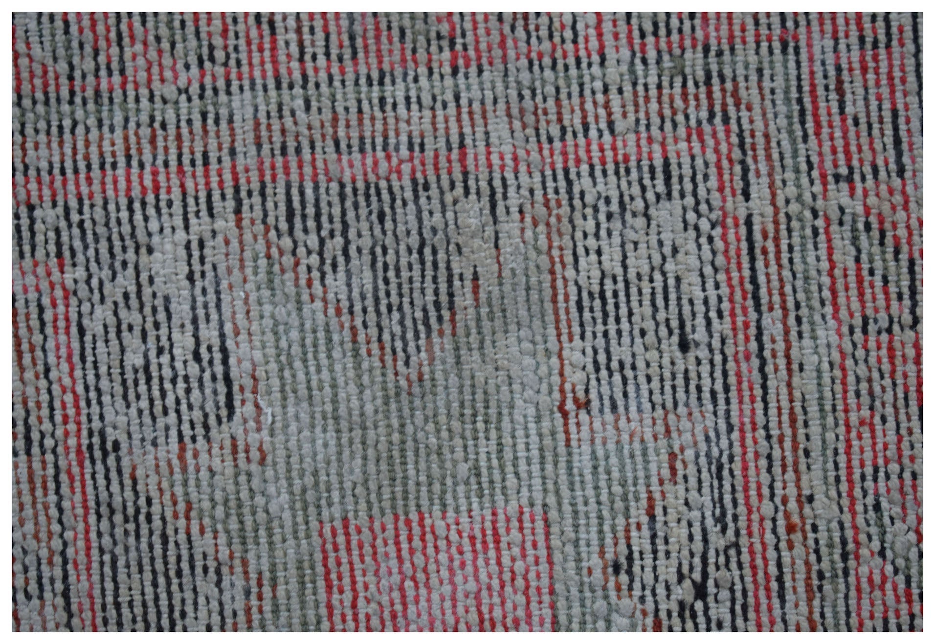 A close-up of a handwoven vintage Persian rug featuring a faded geometric pattern in red and grey.