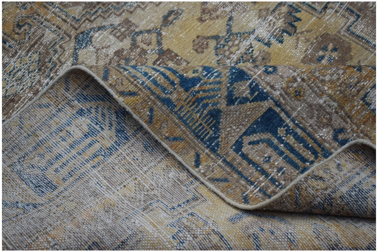 A folded vintage Persian rug featuring a distressed pattern in shades of blue, gold, and beige.