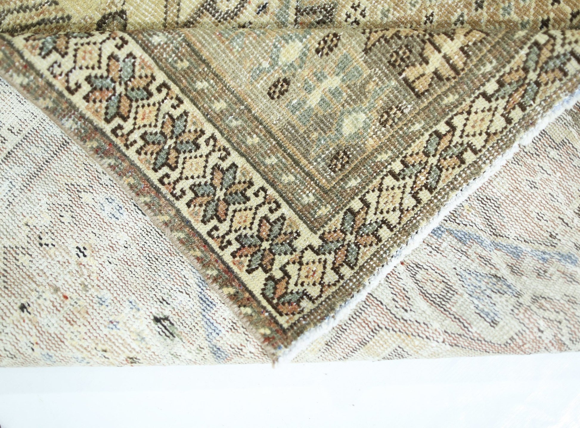 A corner of a vintage Persian Qashqai rug showing its intricate floral border and wool pile.