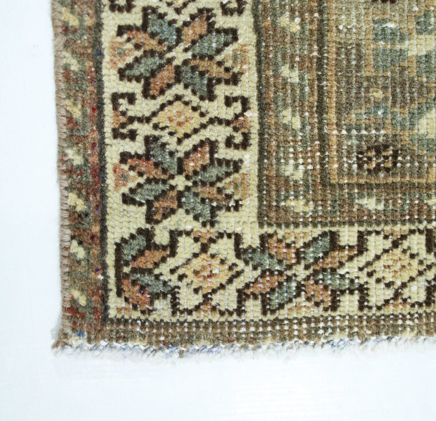 A corner detail of a vintage Persian Qashqai rug featuring intricate floral patterns in muted tones.